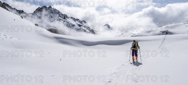 Atmospheric clouds in a wintry mountain landscape, ski tourer on the ascent to Porta d'Es-cha, Bündner Haute Route ski tour, Albula Alps, Rhaetian Alps, Grisons, Eastern Switzerland, Switzerland, Europe