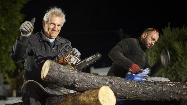 ©Udo Rein, An elderly man gives a thumbs up while sitting next to a woodworker with a chainsaw, Easter bonfire Psinthos, Holy Saturday, Easter, Psinthos, Rhodes, Dodecanese, Greek Islands, Greece, Europe