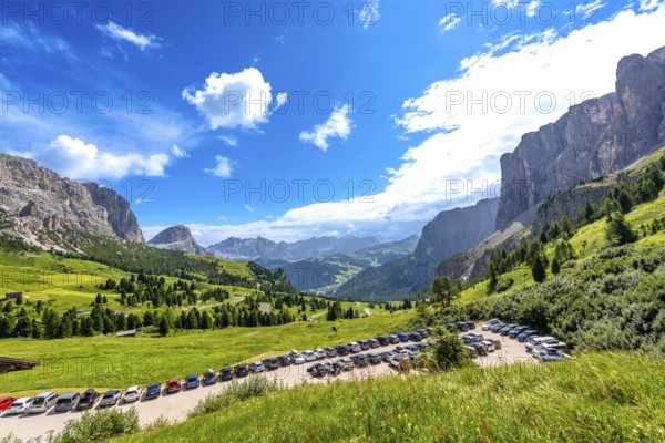 Cars parked near gardena pass with breathtaking views of the dolomites mountains in a sunny summer day