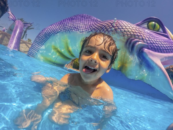 Happy child sticking out his tongue, enjoying playful moments at a vibrant water park during a sunny summer vacation