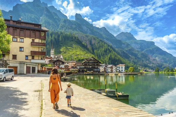 Tourists strolling along the lakefront of alleghe, a charming village nestled in the heart of the italian dolomites, enjoying the stunning mountain scenery on a summer day