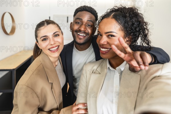 Three cheerful businesspeople taking a selfie, with one making victory sign, celebrating success in modern office