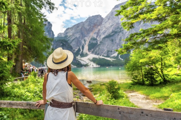 Woman wearing straw hat enjoying majestic view of lake braies - lago di braies or pragser wildsee - and seekofel mountain in dolomites, italy