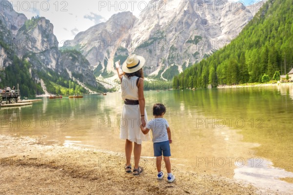 Mother pointing at the landscape while holding her son's hand on the shore of lake braies in the italian dolomites during summer
