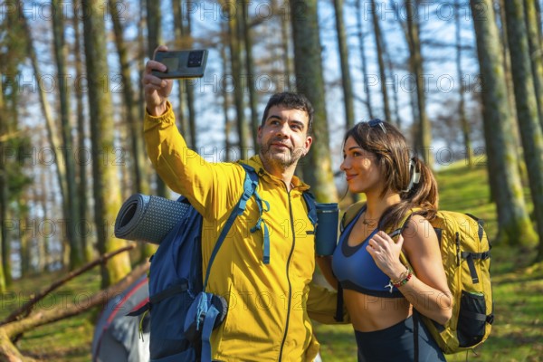 Couple taking a selfie with smartphone in the woods during camping trip, wearing backpacks and casual clothing