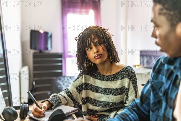 Two graphic designers working from home sitting on a sofa brainstorming, taking notes and discussing new ideas