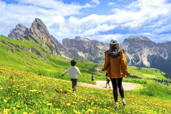 Tourists enjoying a sunny summer day walking through fields of wildflowers in seceda, dolomites, italy
