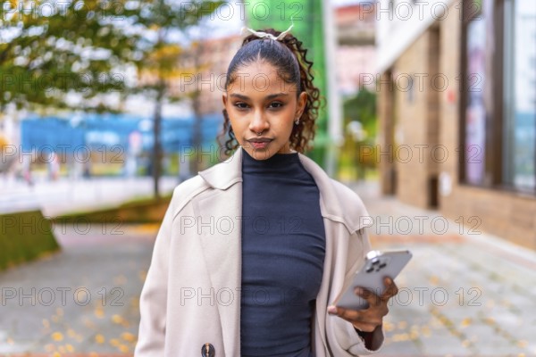 Portrait of a beauty african american woman looking at camera, using phone outdoors in the city