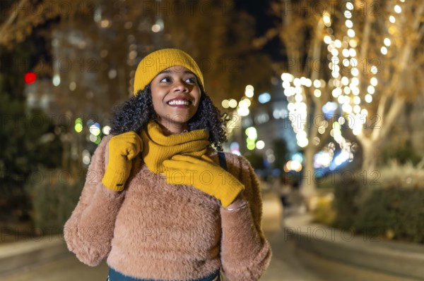 Smiling woman wearing winter clothes enjoying christmas lights decorating city trees at night