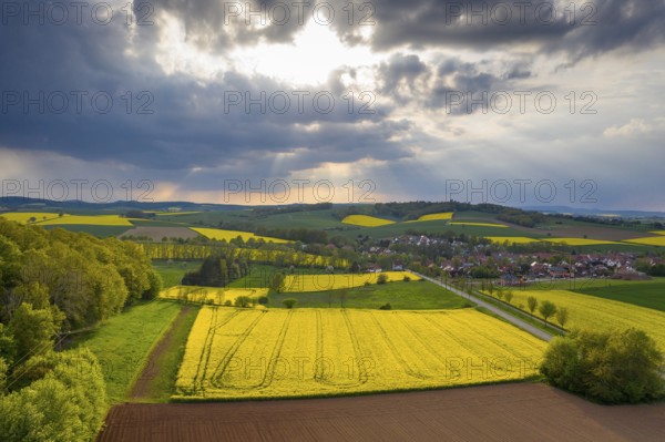 View of Tiftlingerode between blooming rape fields in rain and sunshine, Duderstadt, Lower Saxony, Germany, Europe