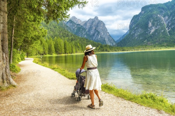 Tourist walking with her baby along the scenic shores of lake dobbiaco, surrounded by the stunning dolomite peaks in italy