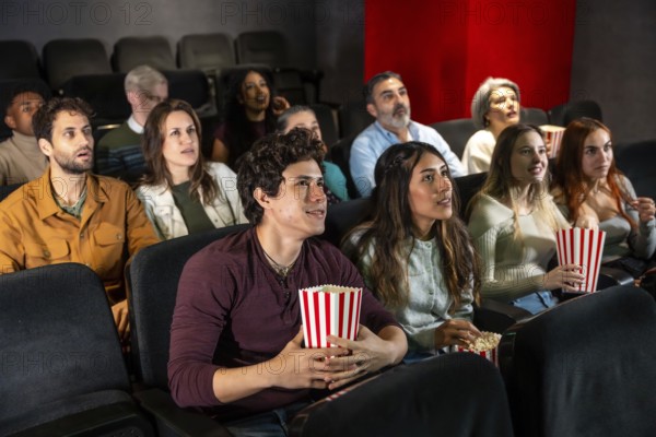 People of different ages and ethnicities are watching a film in a movie theater, holding popcorn buckets and enjoying the show