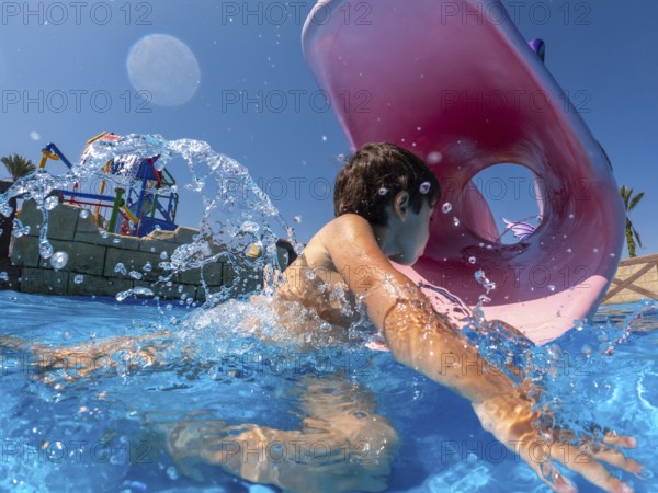 Child having fun swimming through inflatable ring in water park during summer vacation, enjoying refreshing splash in mediterranean sea