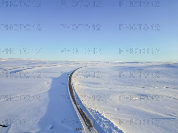 Beautiful aerial drone view landscape. Frozen road in winter in Iceland. Snowy roadsides during winter with blue sky