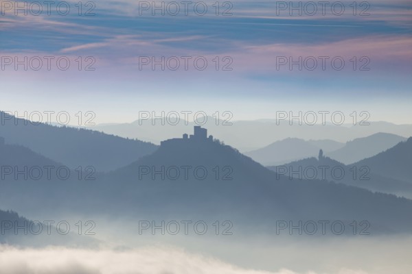 Autumnal panorama of the Palatinate Forest with mountain peaks and valleys in the mist. Trifels Castle near Annweiler can be seen in the centre of the picture
