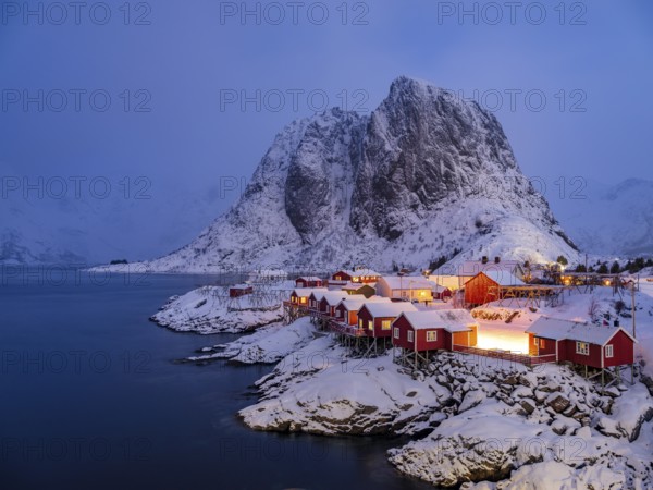 Rorbuer huts of Hamnoy at the fjord at dusk, snowy mountains in the background, Hamnøy, Reine, Moskenesøya, Lofoten, Norway, Europe