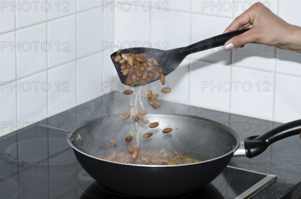 Woman Hand Holding and Using a Big Spoon to Cooking Beans with a Frying Pan in Kitchen in Switzerland