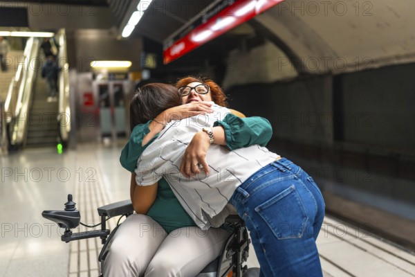 Joyful woman hugging a disabled friend in wheelchair in the subway while waiting for the metro