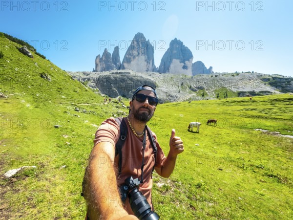 Photographer taking a selfie with thumbs up sign while hiking on a trail in tre cime di lavaredo, dolomites, italy