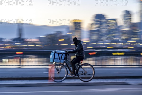 Skyline of the city centre of Frankfurt am Main, cyclist on the Flößerbrücke, Wolt delivery service, dusk, river Main, winter, Hesse, Germany, Europe