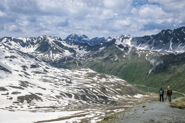 Stilfserjoch, Vinchgau, South Tyrol, Italy -Hiker on a hiking trail above the Stilfser Joch pass road, summit of the pass road, snow-covered mountain landscape of the Swiss Alps in the background