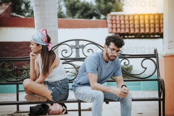 Unhappy couple sitting back to back on bench. Concept of couple problems and crisis. Upset young couple sitting back to back in a park, Young couple arguing sitting back to back on a bench