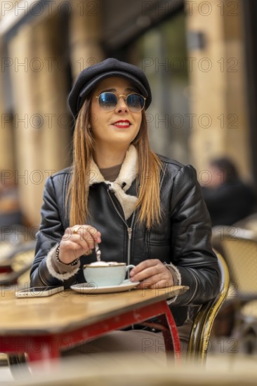 Fashionable woman wearing sunglasses and a hat savoring a cappuccino at a parisian cafe, enjoying the european atmosphere