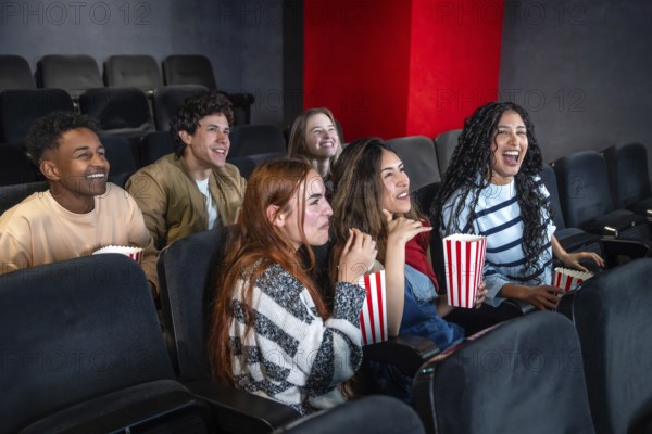 Group of young people enjoying a movie at the cinema, sharing laughter and smiles while munching on popcorn and having a great time