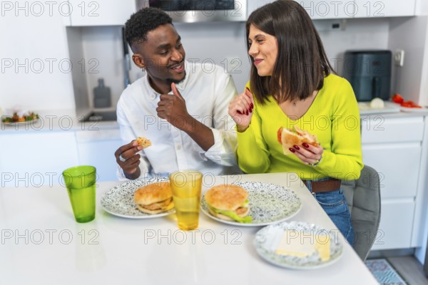 Young multiethnic couple sharing homemade burgers and enjoying each others company in a modern, bright kitchen filled with warmth