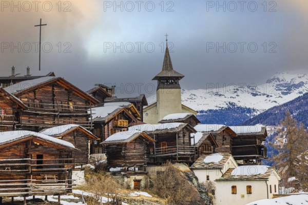 Old wooden houses with snow-covered roofs and the Saint Theodule church in the historic village centre, Grimentz, Val d'Anniviers, Valais Alps, Canton Valais, Switzerland, Europe