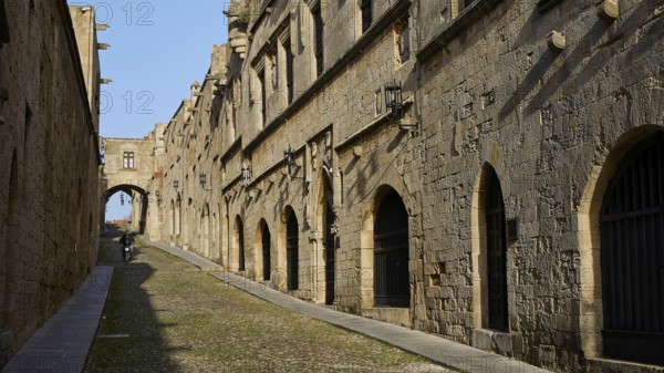 An ancient street lined with historic buildings with arcades in sunny weather and blue skies, moped riders, Knights Street, Rhodes Old Town, Rhodes Town, Rhodes, Dodecanese, Greek Islands, Greece, Europe