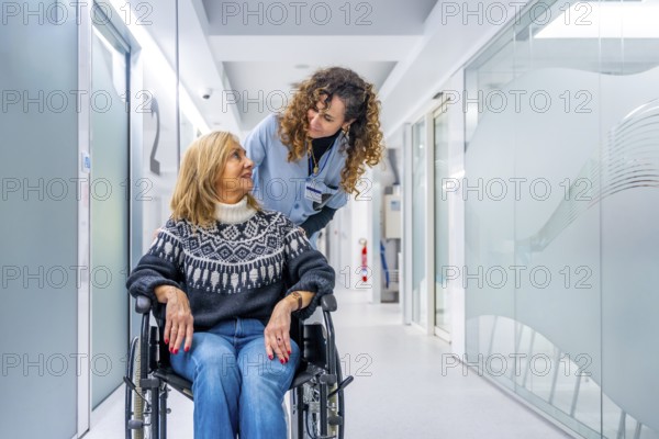 Young tender nurse talking to a mature injured woman in wheelchair in the hospital