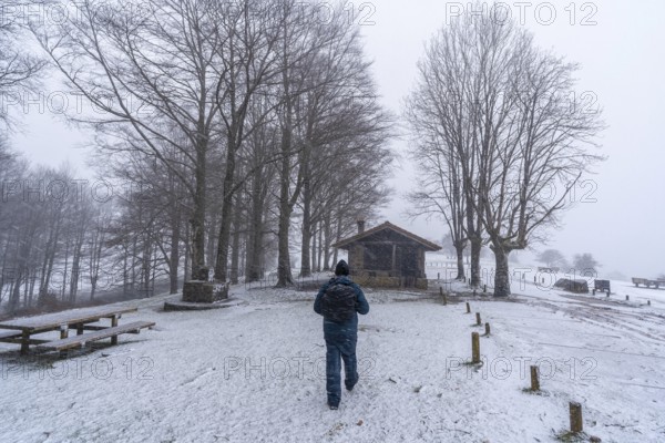 A young man walking next to the refuge of mount aizkorri in gipuzkoa. Snowy landscape by winter snows. Basque Country, Spain, Europe