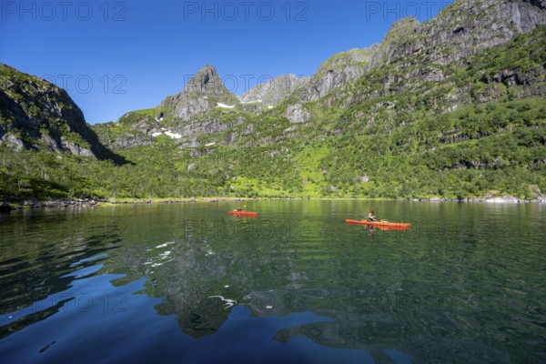 Two kayakers with red kayaks in the fjord Trollfjord, mountain peaks are reflected in the water, fjord landscape and mountains, Lofoten, Nordland, Norway, Europe