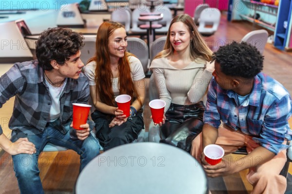 Four young friends enjoying a casual hangout at the bowling alley, holding red cups and engaging in lively conversation