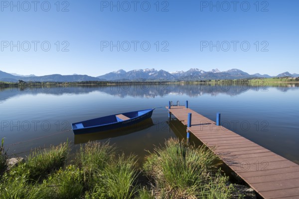 Blue sky over an alpine lake with a boat and a jetty, surrounded by mountains, Hopfen am See, near Füssen, Ostallgäu district, Swabia, Bavaria, Germany, Europe
