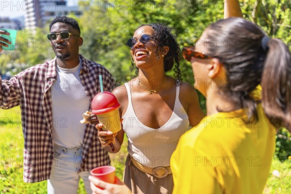 Cheerful group of friends laughing, dancing, and enjoying refreshing drinks in a vibrant park setting