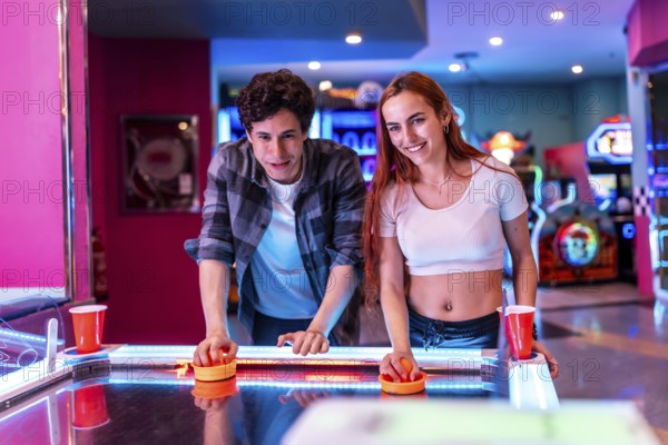 Multiethnic friends enjoying a weekend together, playing air hockey in a vibrant entertainment center filled with arcade games and colorful neon lights