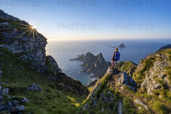 Mountaineer on the summit of Måtind or Måtinden, view of picturesque coastal landscape with sun star, rocky coast and sea, Andøya Island, Vesterålen, Nordland, Norway, Europe
