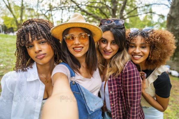 Four cheerful young women smiling and taking a selfie in a park, enjoying their time together in the vibrant outdoors