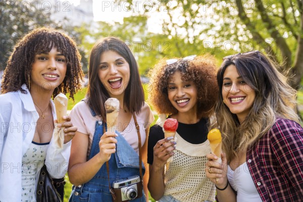 Four cheerful young women enjoying ice cream cones together in a park, celebrating summer and friendship