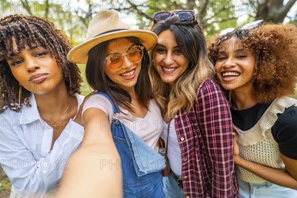 Four young women smiling and capturing a joyful selfie in a park, celebrating their friendship and enjoying a carefree moment together