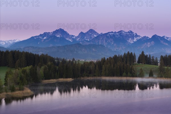 Alpine panorama with a calm lake and mountains in the background in front of sunrise, Hergratsrieder See, Alps, near Füssen, Ostallgäu, Allgäu, Bavaria, Germany, Europe