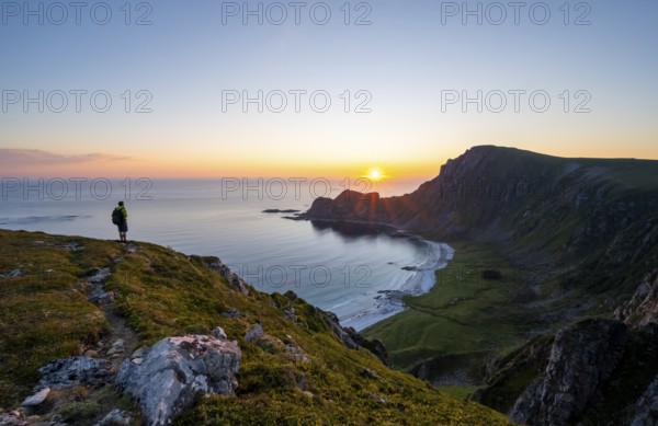 Mountaineer in front of view of coastal landscape at sunset, cliffs and summit of Måtind or Måtinden, Høyvika beach and sea, Andøya island, Vesterålen, Nordland Norway