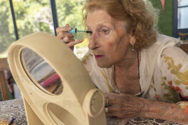 Elderly woman applying mascara with care, using a small mirror on the table, enhancing her beauty routine with precision and focus, embodying self-care and confidence