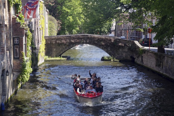 Tourist boat sailing under a historic bridge on a canal, canals, Bruges, West Flanders, Belgium, Europe
