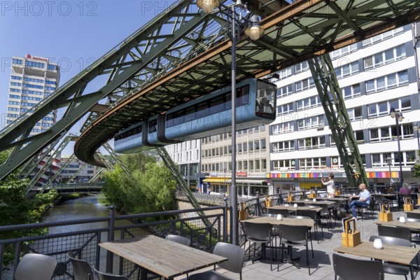 Train of the Wuppertal suspension railway runs along the Wupper, at the main station stop, terrace of a restaurant on a bridge over the river, North Rhine-Westphalia, Germany, Europe