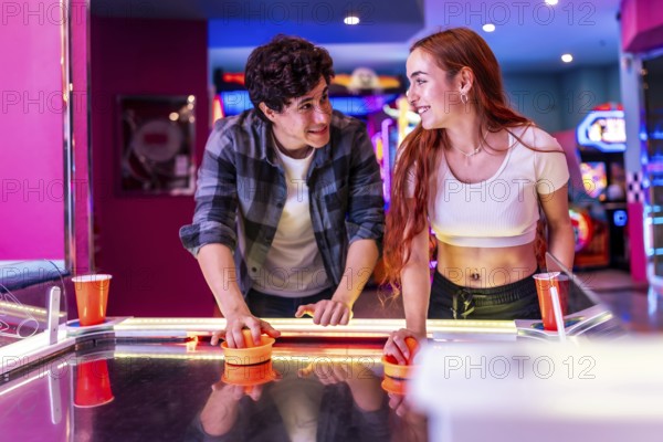 Happy multiethnic friends enjoying a weekend together, playing air hockey in a colorful and dynamic arcade