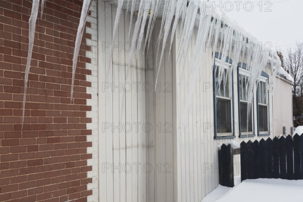 Icicles hanging from snow and ice covered roof of old red brick and white wood plank cladded building in winter, Quebec, Canada, North America
