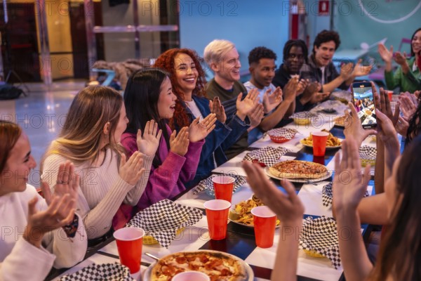 Young diverse people celebrating and having fun together at a bowling alley restaurant, enjoying pizza and snacks while someone takes pictures